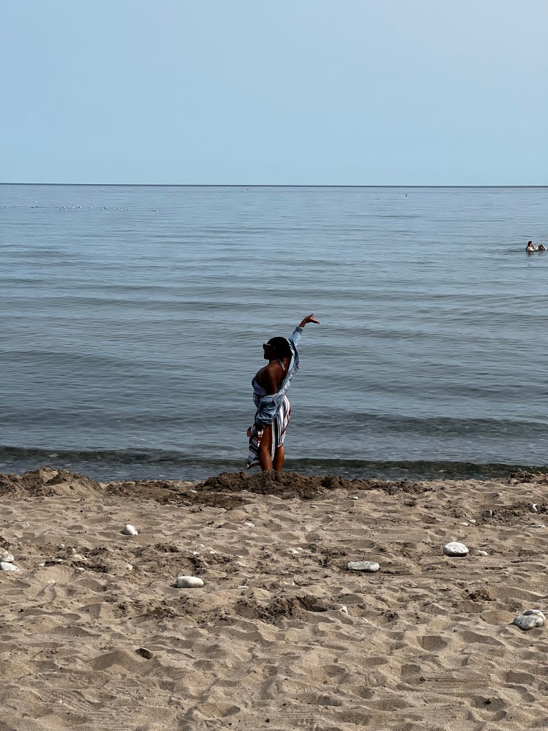 A person stands on a sandy beach, looking out at the ocean waves